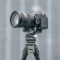 Falcam apvalus pusės raktelis su greito atlaisvinimo mechanizmu, pritvirtintas prie Sony be veidrodžio kameros su dideliu objektyvu ant stovo, iliustruojantis horizontalios ir vertikalios fotografavimo režimų keitimo galimybę