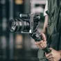 Profesionalinė kamera, sumontuota ant juodo L-braketo su riešo diržu, su dideliu objektyvu ir stabilizatoriaus rankena, skirta Sony ZV E1.