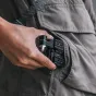 Falcam F22 F38 F50 greito leidimo ir sulankstomas pusės, laikomas rankoje ir dalinai įdėtas į pilką striukės kišenę, rodantis sukamojo mygtuko ir tvirtinimo taškus