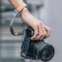 Falcam F22 greito leidimo kameros korpusas Sony A7C, pilkas spalvos aliuminis, pritvirtintas prie kameros, ranka laiko su tan spalvos odiniu dirželiu, matomas nuimamas šoninis skydelis