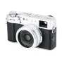 Sidabrinis JJC LH-JX100VII objektyvo gaubtas su adapteriu, pritvirtintas prie Fujifilm X100 serijos kompaktiško fotoaparato, demonstruojantis matinį aliuminio saulės skydelį, saugantį objektyvą.