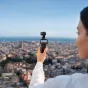 DJI Osmo Pocket 4 Creator Combo kamera su stabilizatoriumi ir mikrofonu, laikoma rankoje su ekranu, rodančiu miesto peizažą, kompaktiška veiksmo kamera su 4K vaizdo įrašymu ir pažangia stabilizacija