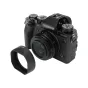 JJC LH JXF23M2 juodo objektyvo apsauga Fujifilm XF 23mm/27mm objektivams su magnetiniu tvirtinimu, išdėstyta šalia Fujifilm be veidrodžio fotoaparato.
