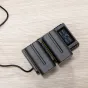 Nitecore NP F Pro komplektas su dviem 5200mAh Sony NP F baterijomis ir USB įkrovikliu, ekranas rodo įkrovimo būseną, įtampą, srovę ir talpą