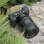 Viltrox AF 35mm F1.2 LAB objektyvas Sony E-mount su ultragausiu atviru ir aukštos kokybės konstrukcija, įmontuotas į kamerą ir rodomas lauko aplinkoje ant tekstūruoto akmens paviršiaus su žaliais augalais fone.