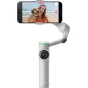 Insta360 Flow 2 Pro AI Tracker naudojamas su išmaniuoju telefonu, filmuojantis selfį su moterimi ir šunimi paplūdimyje, rodantis 3-ašių stabilizaciją ir kompaktišką dizainą.