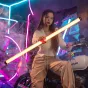 Viltrox K90 dvigubo RGB šviesos lazdelė skleidžia ryškią geltoną šviesą, laikoma horizontaliai žmogaus kasdieniame drabužyje, apsupta neoninių šviesų ir dūmų efektų, pabrėžiant jos elegantišką dizainą ir nešiojamumą.