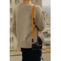Peak Design Form Leather kameros diržas amber spalvos su žemaprofiliais Anchor Link jungtimis, elegantiškai užmesta per megztą džemperį, sukuriant stilingą ir minimalistinį įvaizdį