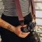 Peak Design Slide Lite fotoaparato diržas su Anchor Link tvirtinimo sistema, pritvirtinta prie be veidrodinės kameros, matomas glotnus rudas diržo audinys ir dvigubi greito reguliavimo mechanizmai.