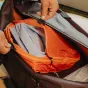 Peak Design Packing Cube Medium oranžinė ir juoda su atskiriama UltraZip, atidarytas, kad būtų matomi du skyriai švariems ir nešvariems drabužiams.