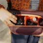 Peak Design Everyday Sling V2 3L krepšys atidarytas vaizdoje su fotoaparato objektyvu viduje, rodantis paminkštintas skirstikles ir kompaktišką talpyklą kelionių fotografijos įrangai