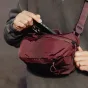 Peak Design Outdoor Sling 4L raudona spalva su oru apsaugine Terra Shell medžiaga, rodomas reguliuojamos diržo sistemos ir magnetinė uždarymo priekinė kišenė.