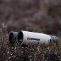 GPO 8x32ED binokliai su magnio korpusu, vandeniui atsparia konstrukcija ir ED lęšiais, ilsintis ant rudų viržių augalų su baltais žiedais.