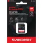 SanDisk Extreme PRO 64GB SDXC UHS-I atminties kortelė prekybos pakuotėje su fotoaparato objektyvu fone