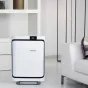 BONECO P500 Oro valytuvas su elegantiška balta priekinė panelė ir juoda apdaila, eksponuojamas moderniame svetainėje šalia baltos sofos, turi skaitmeninį ekraną ir HEPA filtrą, pašalinantį žiedadulkes, dulkių erkutes ir kvapus