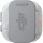 DJI MIC MINI 2S siųstuvas skaidriame apsauginiame korpuse, priekinis vaizdas su iškilusiu DJI logotipu, įjungta žalia indikacija, kompaktiškas bevielis lavalier mikrofonas.
