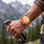 Tech-Protect oranžinė nailono apyrankė Huawei Watch Fit serijai, kvėpuojanti ir reguliuojama, dėvima ant prakaituoto riešo, laikant žygių lazdą kalnų fone.