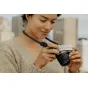 Peak Design Form Rope Neck juosta juoda apvijasi aplink moters kaklą, kai ji laiko Fujifilm X‑E5 be veidrodinę kamerą, pabrėždama minimalistinį nailoninį virvės dizainą ir žemo profilio greito atlaisvinimo tvirtinimus.