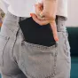 Moteris su oranžiniu manikiūru įdeda ploną juodą Peak Design Passport Wallet į šviesių džinsų užpakalinę kišenę, demonstruodama jo RFID apsaugą ir magnetinį užsegimą.